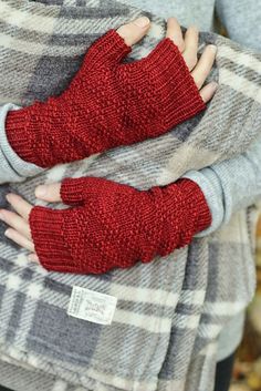 a woman wearing red knitted mitts while standing in front of a plaid blanket