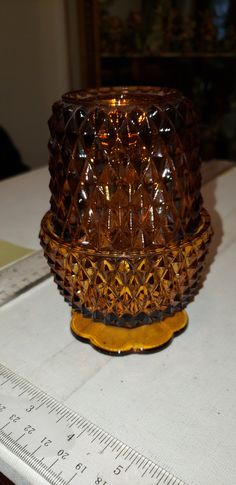 a brown glass vase sitting on top of a table next to a measuring tape and ruler