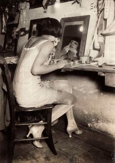 an old black and white photo of a woman sitting in front of a mirror brushing her teeth