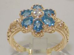 "Six very colorful pretty Gemstones all hand set into this delightful Solid 14K Yellow Gold Antique style Flower setting, which has a Stunning unusual Art Nouveau design carved into the shoulders. One central Sparkling Cubic Zirconia, 3mm round (0.11\") surrounded by six Vibrant Blue Natural Topaz, oval cut 4x3mm (0.16\" x 0.12\"). The sparkle of these gemstones and their contrast with the Polished Gold is just so eye catching you just can't stop looking at this ring on your hand. These are Genu Rings Pandora, Unusual Art, Art Nouveau Design, Art Nouveau Style, Ring Sizes, Jewelry Wedding, Fine Rings, Sparkle Diamonds, Diamond Art