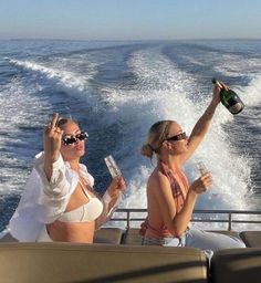 two women in bikinis are on a boat drinking champagne and holding up their hands