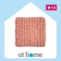 a pink knitted pillow sitting on top of a blue and white background with the words at home written below it