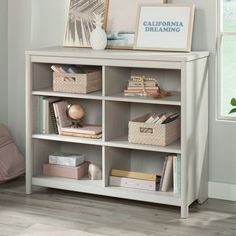 a white book shelf with baskets and pictures on top