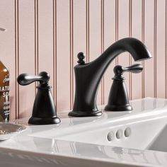 two black faucets sitting next to each other on a white counter top in front of a pink wall