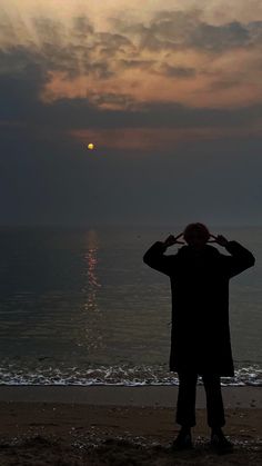 a man standing on top of a beach next to the ocean under a cloudy sky