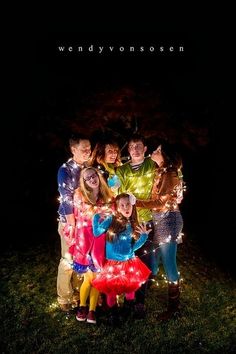 a group of people standing next to each other in the grass with lights on them