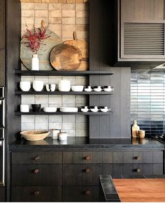 a kitchen with black cabinets and white dishes on the counter top, along with wooden shelves