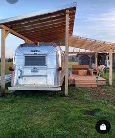 an old trailer is parked under a wooden awning in the grass next to a picnic table