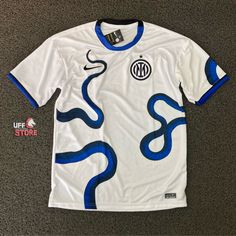 the soccer jersey is white with blue swirls on it and has a black stripe down the chest