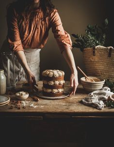 a woman cutting a cake on top of a wooden table next to bowls and utensils