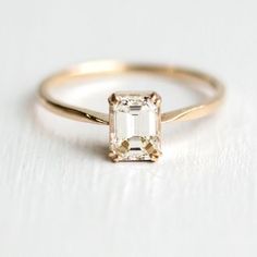 a gold ring with an emerald cut diamond in the center on a white table top