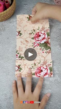 two hands are holding a piece of paper with flowers on it and yarn in the background