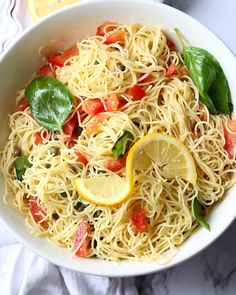 a white bowl filled with pasta, tomatoes and spinach on top of a table