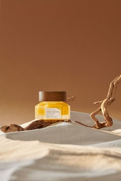 a bottle of yellow liquid sitting on top of a white cloth covered bed next to a twig