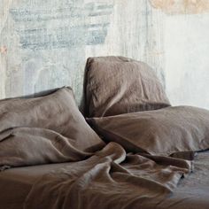 a bed with brown sheets and pillows in front of an old wooden headboard that has peeling paint on it