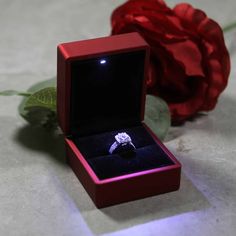 a red box with a ring in it sitting next to a flower and a rose