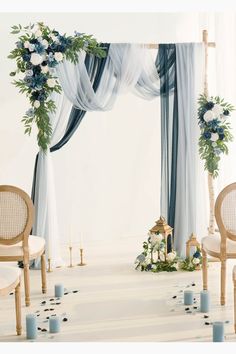 a white and blue wedding arch with flowers, candles and greenery on the floor