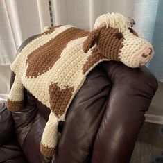 a crocheted cow blanket sitting on top of a brown leather chair