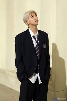 a young man wearing a suit and tie standing in front of a white wall with his hands in his pockets