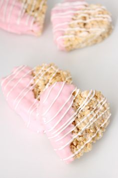 three heart shaped cookies with pink icing and sprinkles on white surface