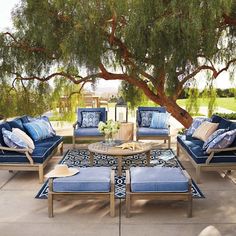 an outdoor seating area with blue cushions and pillows on the floor, under a tree