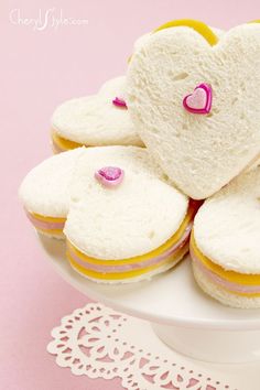 several heart shaped sandwiches on a plate with pink and yellow trim around the edges, sitting on a lace doily