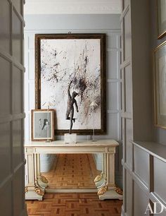 a painting hangs on the wall above a console table in an entryway with hardwood floors