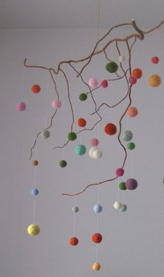 a mobile made out of felt balls hanging from a tree branch in a white room