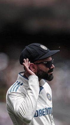 a man wearing sunglasses and a black hat is holding his hand up to his ear