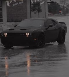 a black sports car driving down a wet street in the middle of the day with lights on