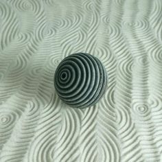 a round object sitting on top of a white bed sheet covered in ripples and circles