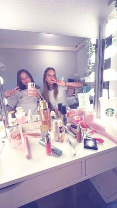 two young women taking selfies in front of a mirror with makeup and cosmetics on the counter