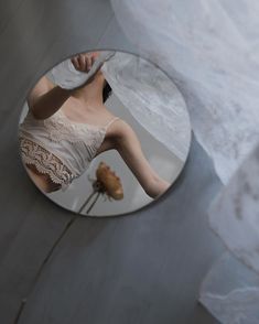 a woman's reflection in a round mirror on the floor next to a flower