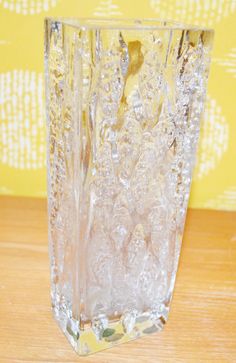 a clear glass vase sitting on top of a wooden table next to a yellow wall