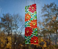 a stained glass sun catcher hanging from a string in front of trees and blue sky