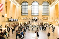 many people are standing in the lobby of a train station with high ceilings and large windows