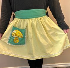 a woman wearing a yellow dress with a green apron on her waist and the back of her skirt has an image of a cat