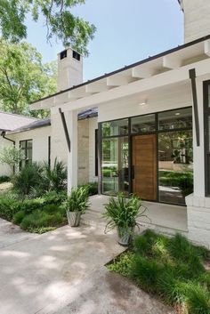 a white house with black trim and wood door, plants in the front yard area