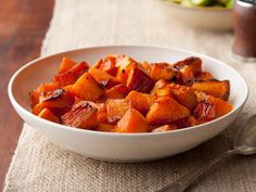 a white bowl filled with sweet potatoes on top of a table next to a spoon