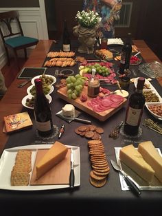 a table filled with cheeses, crackers and other food on plates next to bottles of wine