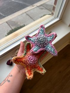 a hand holding a crocheted starfish in front of a window