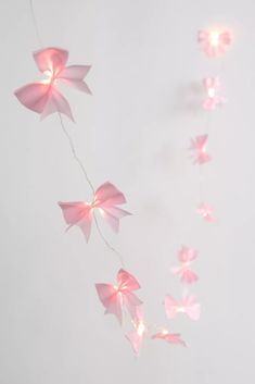 some pink paper flowers are hanging from a string on a white wall with lights in the background