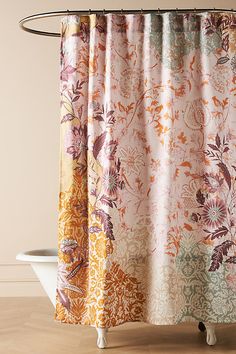 a shower curtain with an orange and pink flower pattern on it, in front of a bathtub