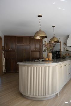 a large kitchen with wooden floors and white counter tops, two pendant lights hanging over the island