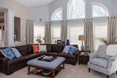 a living room filled with lots of furniture in front of two large windowed windows