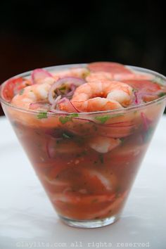 a glass bowl filled with shrimp salad on top of a white table next to a fork