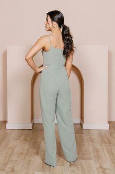 a woman standing in front of a wall with her back to the camera, wearing a green jumpsuit