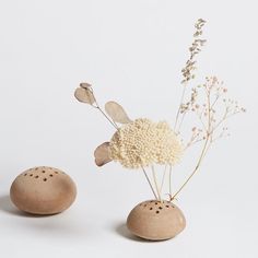 two small vases with flowers in them on a white surface, one is made out of wood