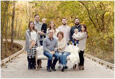 a family poses for a photo on a bridge in the woods with fall foliage behind them