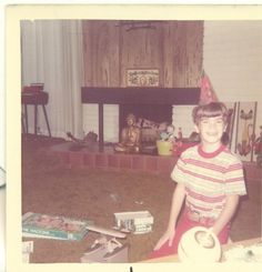 a young boy standing in front of a fireplace with a party hat on his head